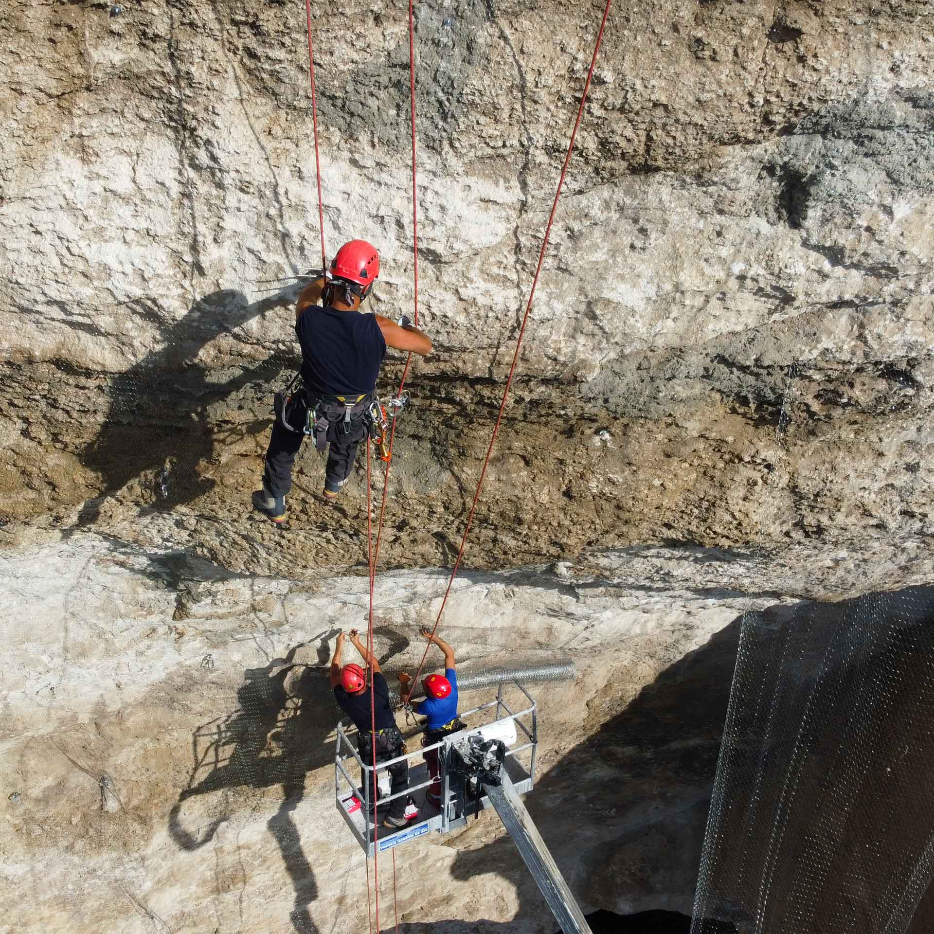 Grotta Cordari e Grotta Salnitro, (SR). Tre rocciatori posizionano rete di contenimento sulla parete rocciosa, fotografia aerea