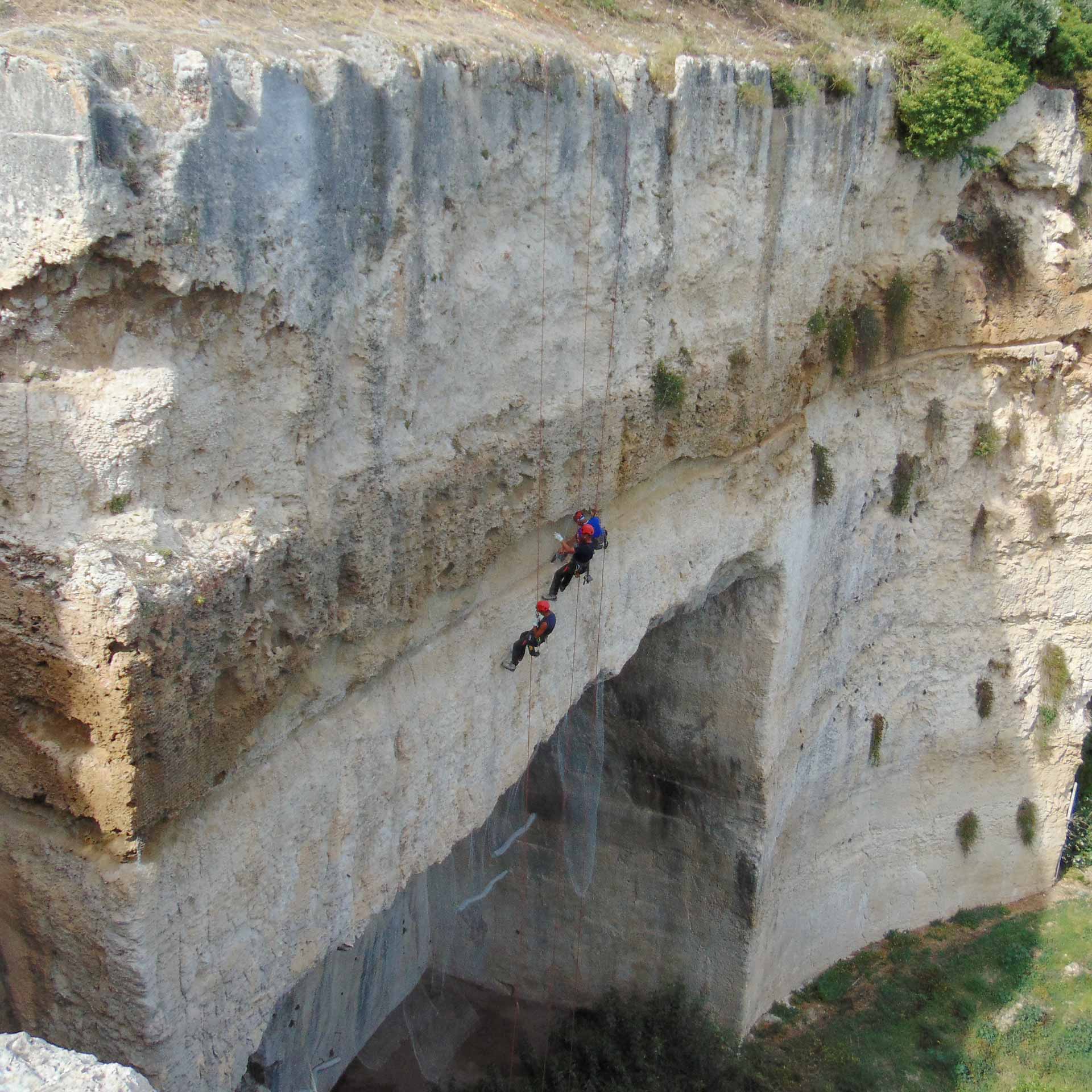 Grotta Cordari e Grotta Salnitro, (SR). Tre rocciatori consolidano parete rocciosa posizionando rete di contenimento, fotografia aerea